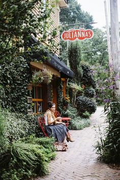 a woman sitting on a red bench in front of a building with plants growing around it