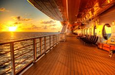 the deck of a cruise ship as the sun sets over the ocean in the distance