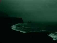 the ocean is very dark and green with waves crashing on it's shore, while two ships are seen in the distance