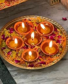 small candles are placed in a bowl with flowers on the floor next to it,