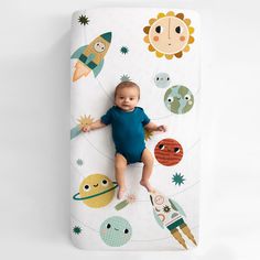 a baby laying on top of a blanket covered in space related images and animals,