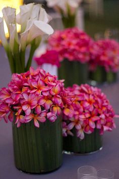 pink and white flowers in green vases on a purple table cloth with wine glasses