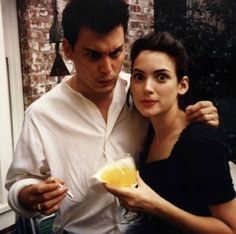 a man standing next to a woman in front of a window holding an orange slice