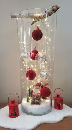 a glass vase filled with ornaments on top of a white cloth covered table next to red candles