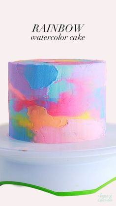 a rainbow cake on a white platter with the words rainbow watercolor cake above it