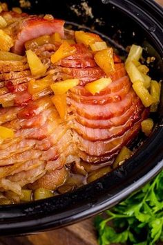 a crock pot filled with ham, pineapples and onions on top of a wooden table