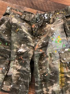 These camo shorts are absolutely perfect.  Side-pocket styling and faded provide a little attitude.  Add to that the paint splatters and you'll be hitting it out of the park. Pair them up with your favorite tee and some flip flops and you're readyfor anything. These are handmade items, so color variations may differ slightly.  #jeanshorts #camo #bermudashorts #splatterjeans #shortsandflipflops #summerfun #summervibes #shopsmall #tiedye #bleachdye #vintagefeel  DETAILS Size: 36 Color: Camo Detail Short Camouflage Cargo Pants, Green White Paint, Outdoor Camouflage Bottoms With Built-in Shorts, Military Camouflage Bottoms For Streetwear, Army Shorts, Military Camouflage Shorts For Streetwear, Army Fatigue, Camouflage Military Cargo Shorts, Military Camouflage Shorts With Side Pockets