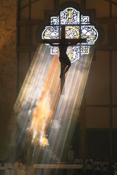 a cross in front of a stained glass window with light streaming through it and people standing around