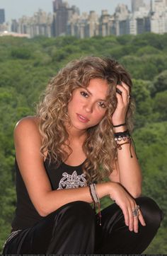 a beautiful young woman sitting on top of a tree covered hillside with trees in the background