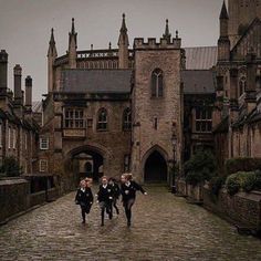 three young boys running down a cobblestone road in front of an old building