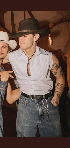 two men in cowboy hats standing next to each other with tattoos on their arms and shoulders