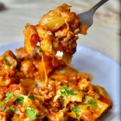 a spoon full of food on top of a white plate with meat and vegetables in sauce