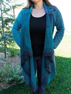 a woman standing in the grass with her hands on her hips, wearing a blue and green knitted cardigan