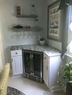 a kitchen with white cabinets and marble counter tops, wine glasses hanging on the wall