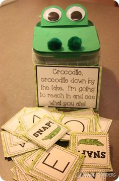 a green frog sitting on top of a pile of cards next to a container filled with words