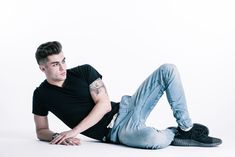 a young man laying on the ground with his legs spread out, wearing jeans and a black t - shirt