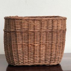 a large wicker basket sitting on top of a wooden table next to a white wall