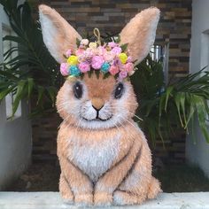 a stuffed rabbit with flowers on its head sits in front of a brick wall and plants