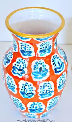 an orange and blue vase sitting on top of a white table next to a yellow rim