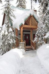 a cabin in the woods with snow on the ground and stairs leading to it's front door