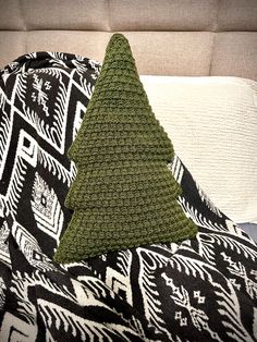 a crocheted christmas tree pillow sitting on top of a bed next to a black and white blanket