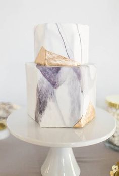 a marble cake with gold accents on a white pedestal and flowers in the back ground