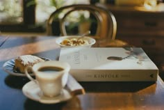 a cup of coffee sitting on top of a table next to a book and plate