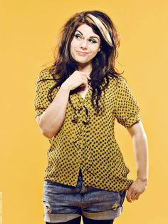 a woman posing with her hand on her hip in front of a yellow background wearing short denim shorts