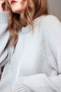 a woman with blonde hair is wearing a white sweater and has her hand on her head