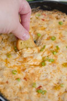 a hand dipping a piece of bread into a skillet filled with cheesy dip