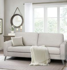 a living room with a white couch and rugs on the floor, windows in the background