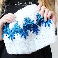 a woman is holding a white and blue crocheted bag with feathers on it