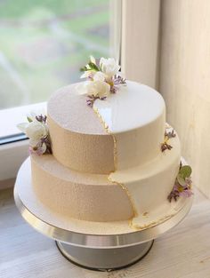 a three layer cake sitting on top of a metal stand next to a glass window