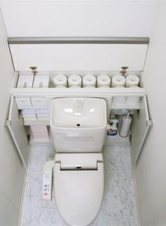 a white toilet sitting inside of a bathroom next to a shelf filled with rolls of toilet paper