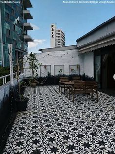 an outdoor patio with black and white tiles on the floor, tables and chairs in front of tall buildings