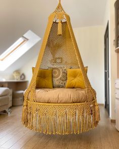 a yellow hanging chair with pillows on it in a room that has white walls and wooden floors