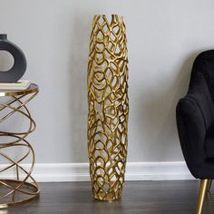 a tall gold vase sitting next to a black chair in a room with white walls