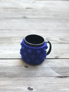 a blue knitted coffee cup holder sitting on top of a wooden table