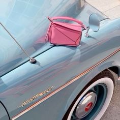 a pink purse sitting on the hood of a blue car