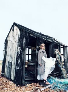 a woman standing in front of a shack on top of a pile of rubble and debris