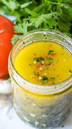 a glass jar filled with yellow liquid next to some tomatoes and parsley on the table