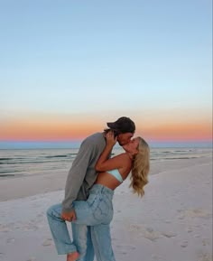 a man and woman kissing on the beach at sunset with ocean in the back ground