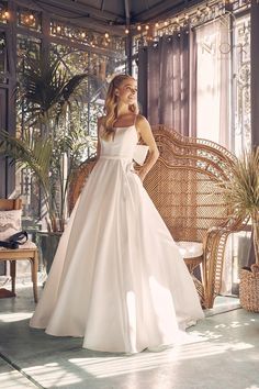 a woman in a white wedding dress standing next to a wicker chair and palm tree