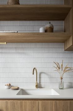 a kitchen with wooden shelves and white counter tops, along with a sink that has a gold faucet