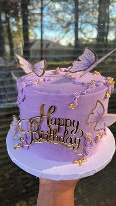 a birthday cake with purple frosting and butterflies on it is being held by a person