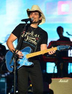 a man wearing a cowboy hat and holding a blue guitar in front of a microphone