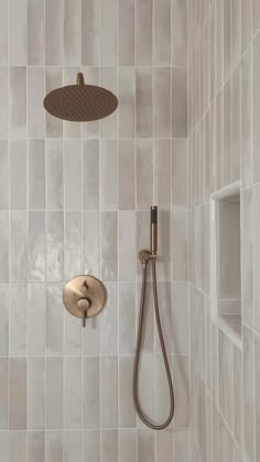 a shower head and hand held shower faucet in a white tiled bathroom with gold accents