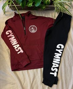 two maroon and black tracksuits sitting on top of a bed next to a potted plant