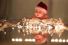 a baby wearing a santa hat sitting on top of a christmas tree with lights in the background