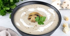 a black bowl filled with soup next to sliced mushrooms and parsley on the side